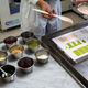 Green and peach-colored Kit Kat chocolate being poured into candy molds beside metal canisters full of ingredients